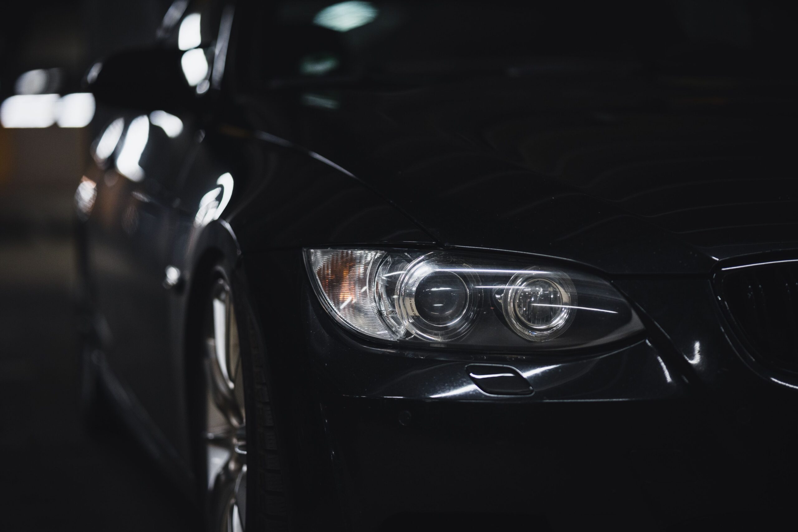 A sleek black sedan with a shining headlight in a dimly lit setting, emphasizing modern automotive design.